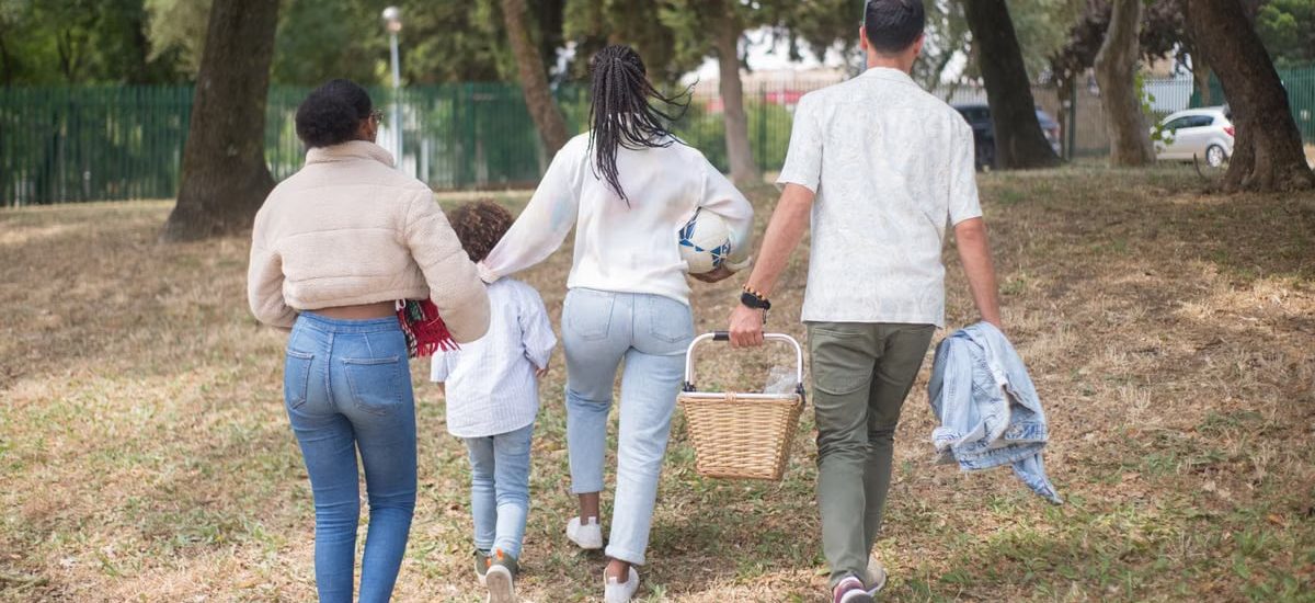 Family walking together carrying picnic basket in a sunny park.