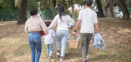 Family walking together carrying picnic basket in a sunny park.