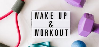Top view closeup composition of wake up and workout inscription on light box surface among expanders and dumbbells and massage ball on white background