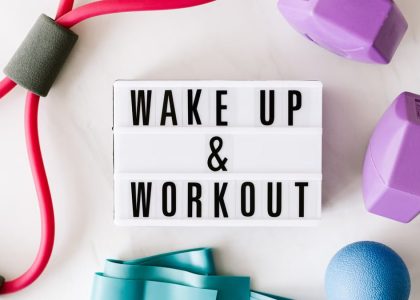 Top view closeup composition of wake up and workout inscription on light box surface among expanders and dumbbells and massage ball on white background